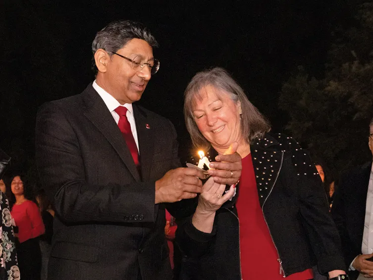 Molly Ranz Calhoun, head of the alumni association, laughs as she leans toward Ohio State President Ravi Bellamkonda to light her candle from one he holds. These are slim, about five inches long and have cardboard circles to keep wax from dripping on their hands. Bellamkonda cups his hand around the flame as he smiles and focuses.