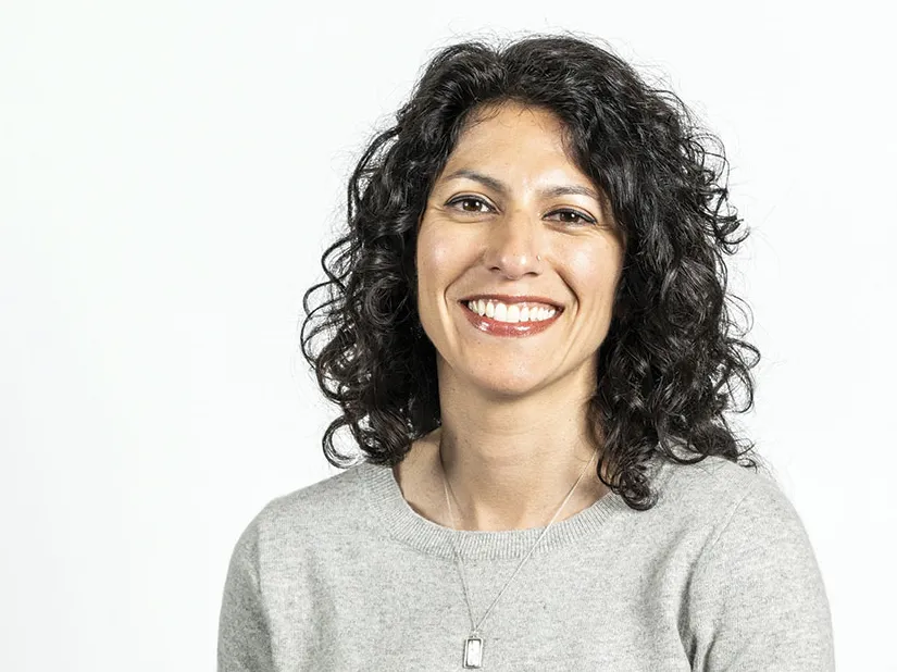 Tahira Rehmatullah smiles as she poses for a photo. She's a pretty woman with curly hair and a big smile.