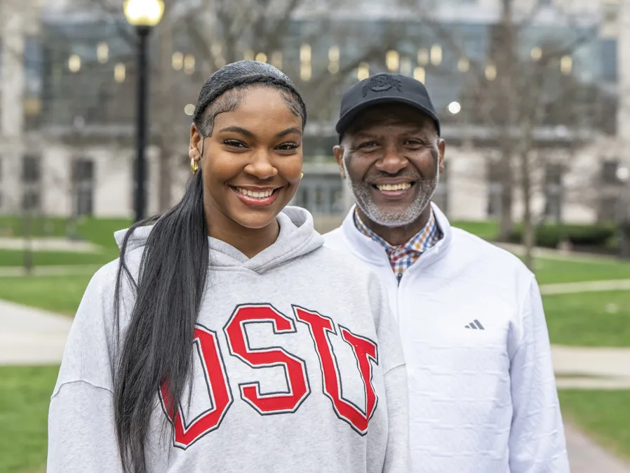 Faith and Keith Hunter smile as they pose on the Oval. Thompson Library is in the background. 