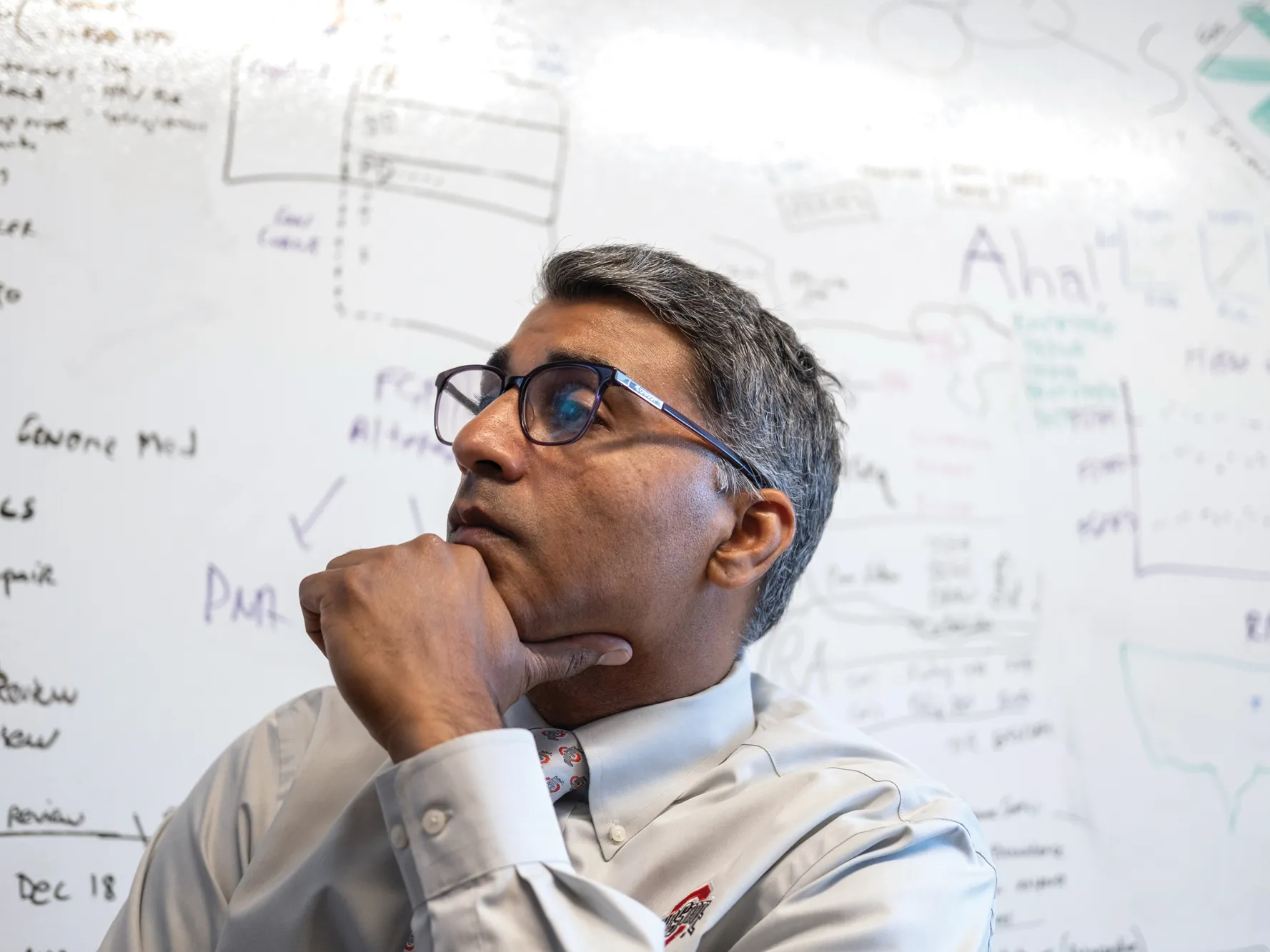Sameek Roychowdhury listens to a remote patient during a meeting in his team's office. Behind him is a white board that has writing all over it.