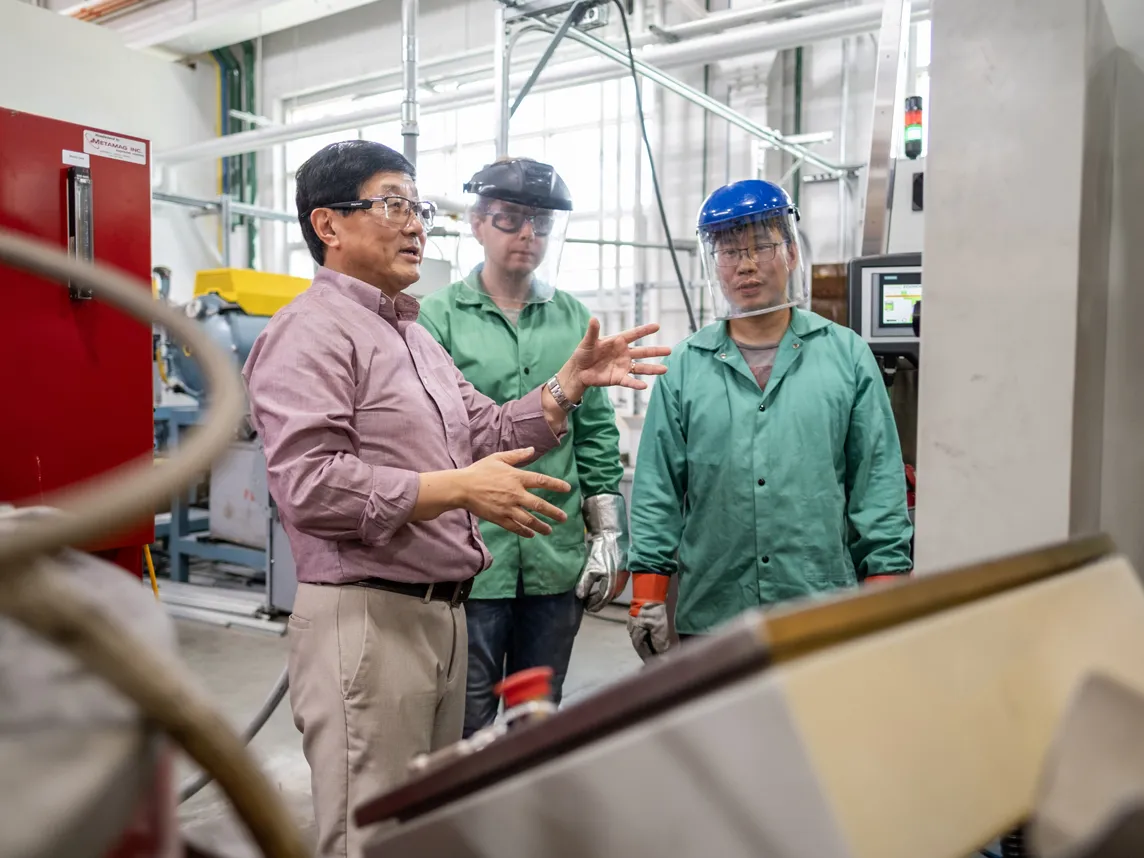 Professor Alan Luo gestures in his manufacturing lab while working with students around big machinery