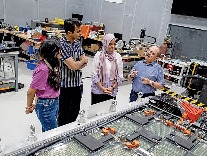 The director of CAR talks with three students in front of a table with a gigantic circuit-board-looking