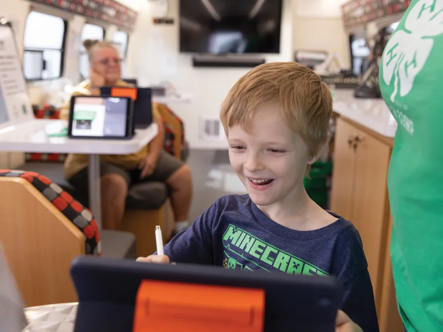 A young boy in a Minecraft T-shirt seems delighted as he works on a tablet computer inside a tech bus from Ohio State