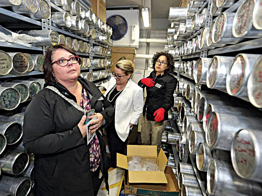 Three women stand between shelves filled with ice cores wrapped in metal. 