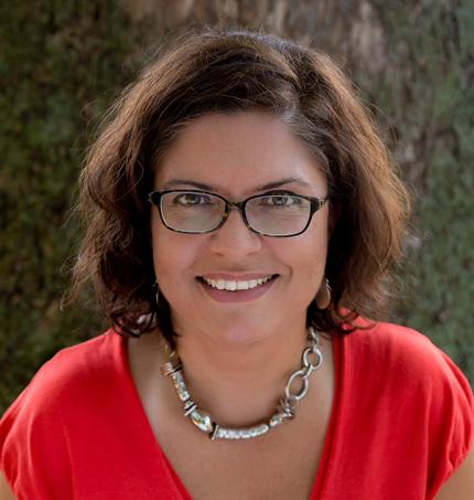 This woman poses for a photo with a pretty smile, glasses and a cool silver necklace. She looks both friendly and like someone who'd make a great friend.