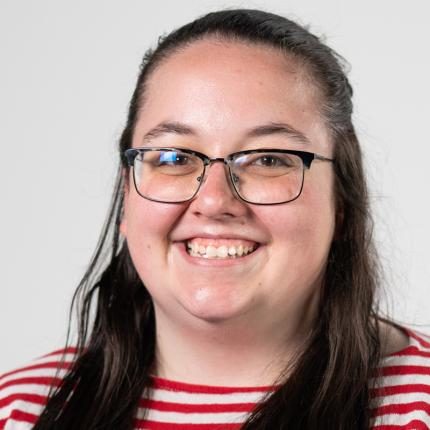 Becca Young smiles in glasses and a scarlet and white striped shirt
