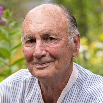 Chuck Hutchison, an older white man in a striped button-down, smiles amid his garden